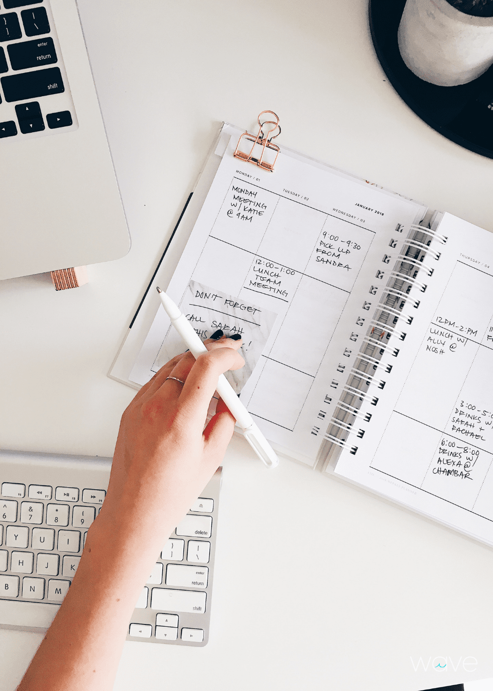 Person it working at a desk. Their hand is showing and they are holding a pen to write into their planner for work.